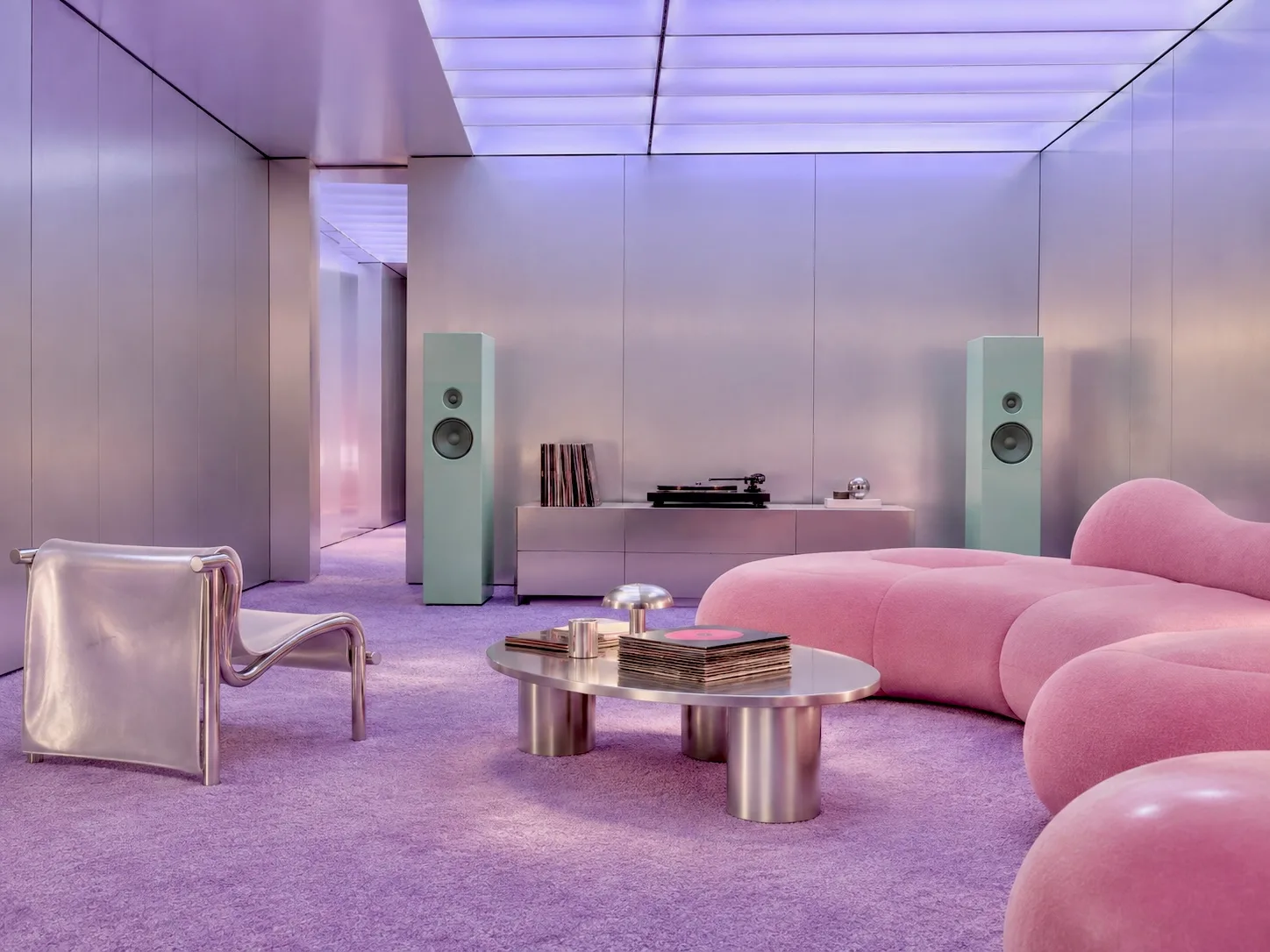 A listening room with brushed metal walls, pink upholstery, a turntable and two speakers