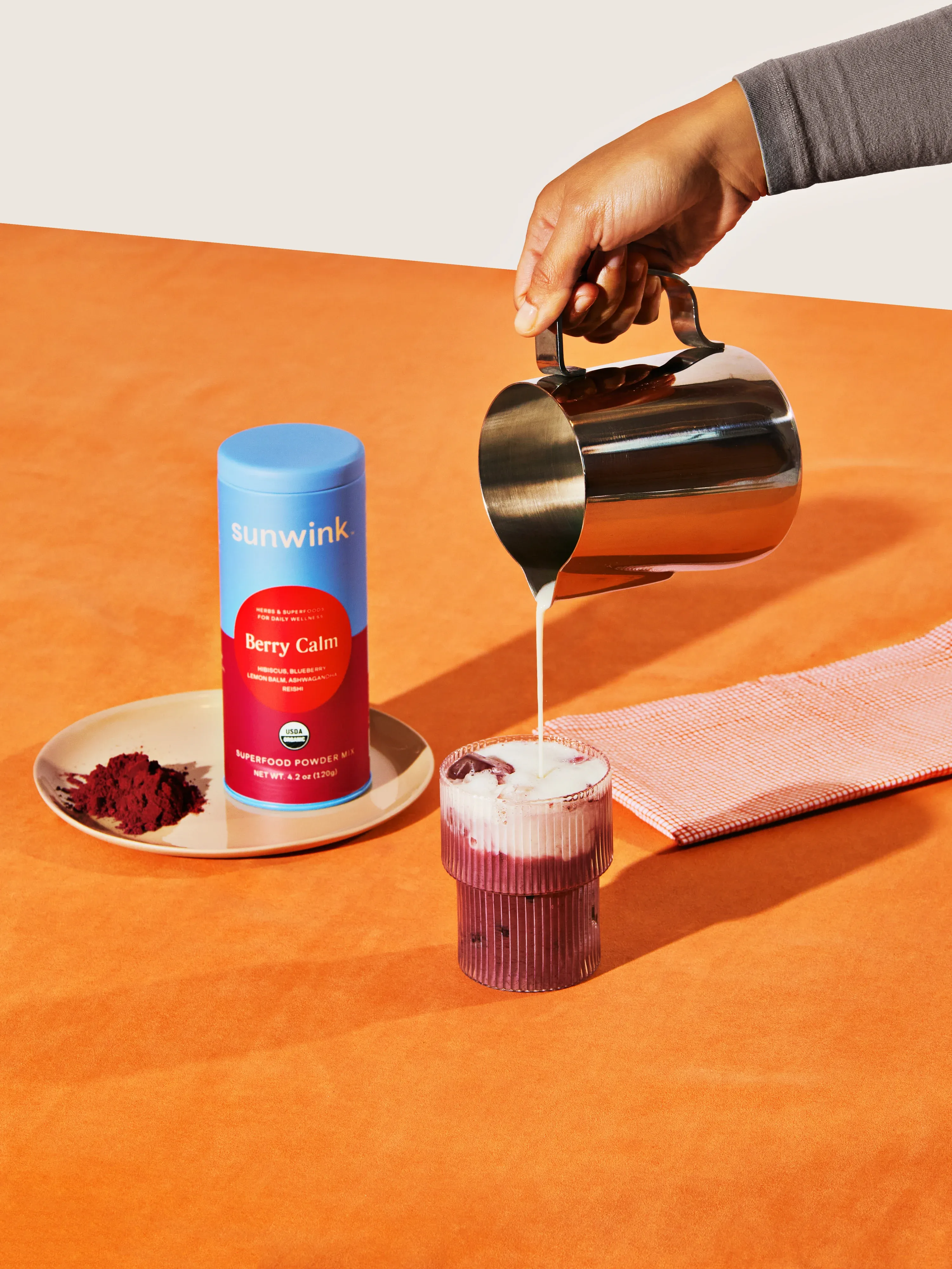 Berry Calm being poured into a glass beside its tin, on an orange table