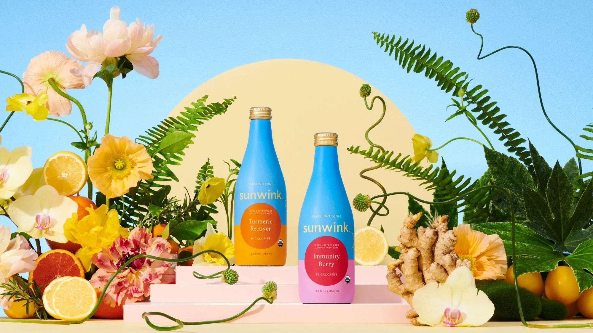 Two Sunwink bottles on pink steps among flowers, ferns, citrus and ginger